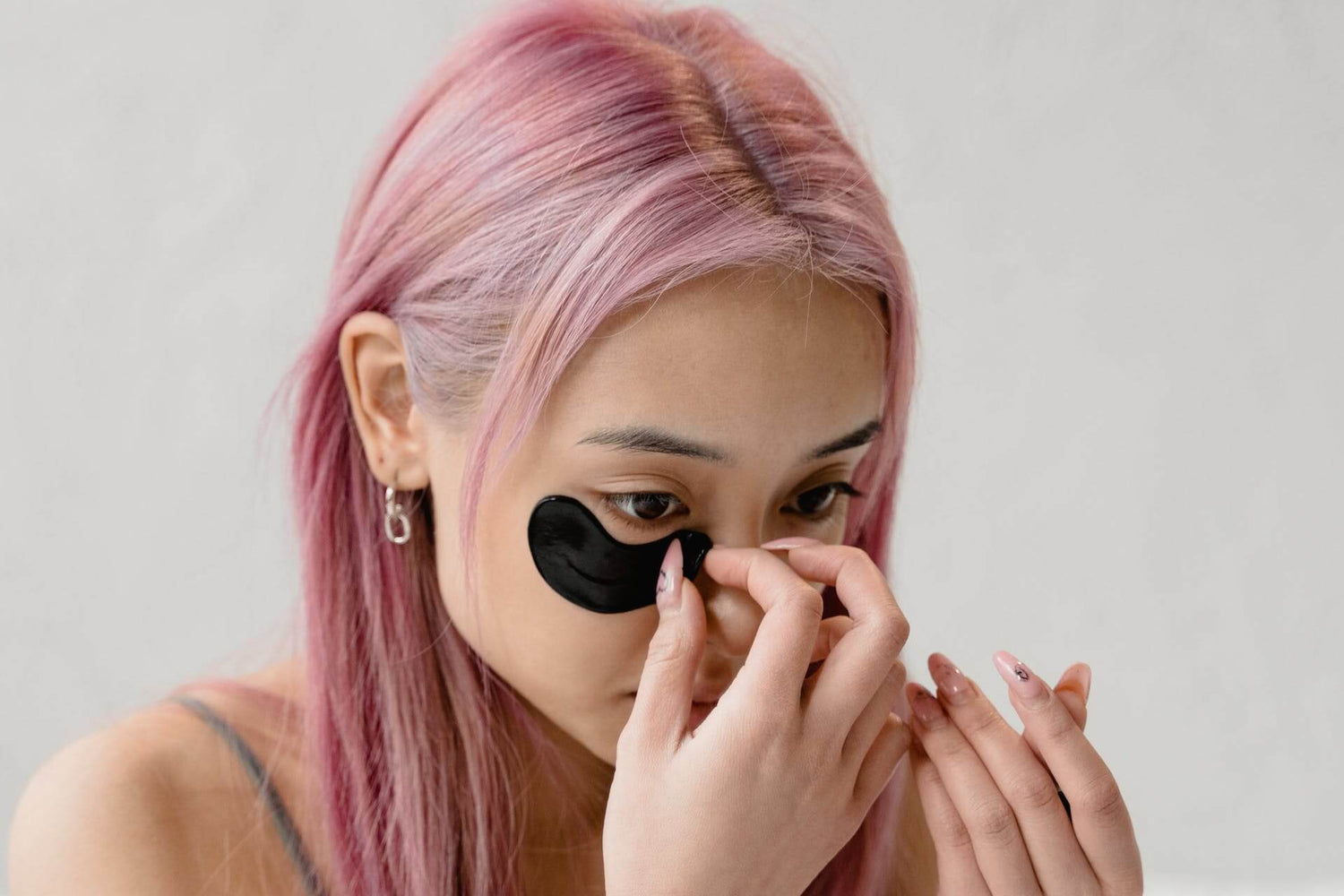 Ragazza dai capelli rosa applica un patch occhi sul viso, come step della skincare routine coreana