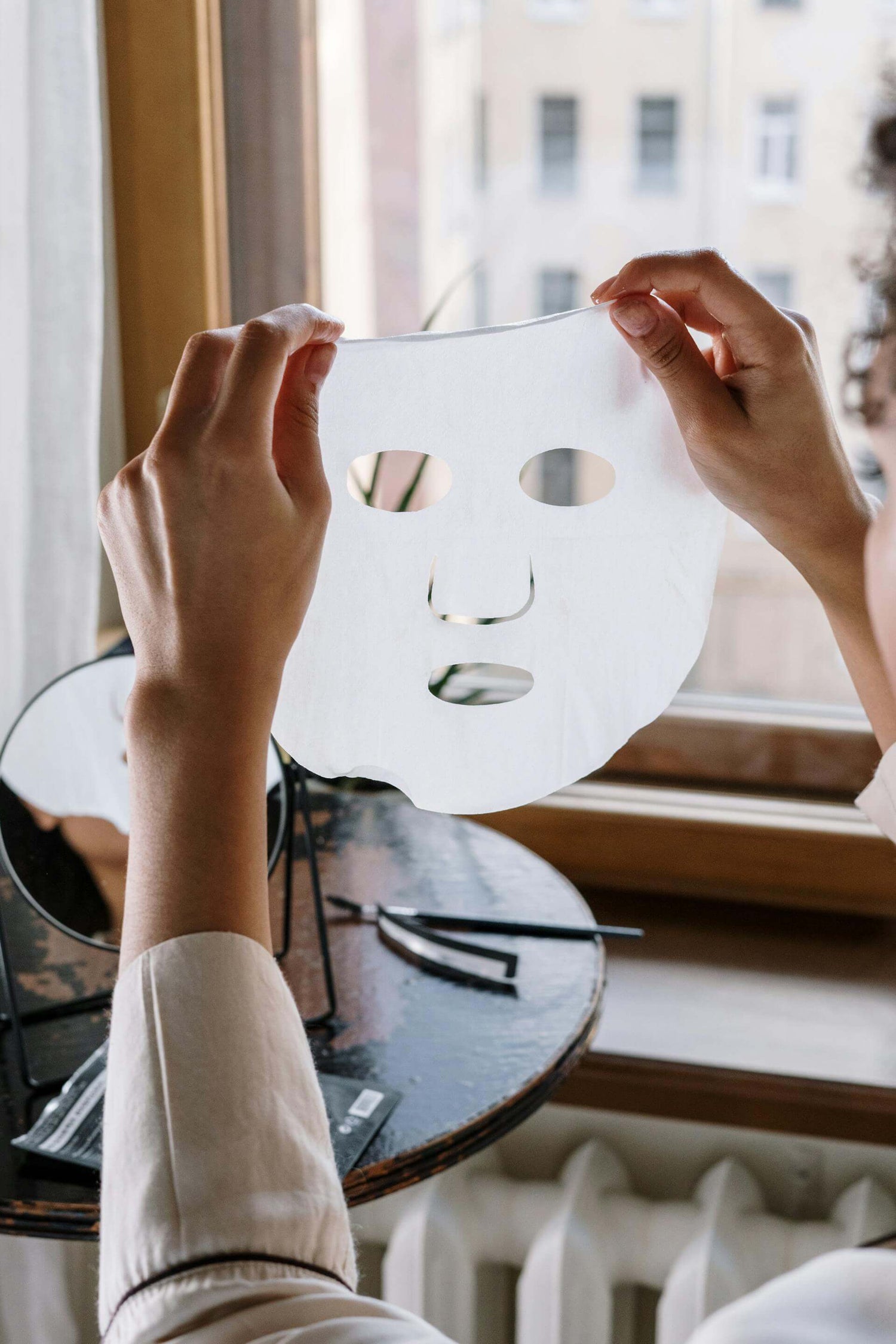 Una maschera viso coreana, in tessuto, tenuta aperta davanti a un piccolo specchio, prima di essere applicata